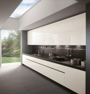 Modern minimalist kitchen with glossy white cabinets dark countertop and skylight.