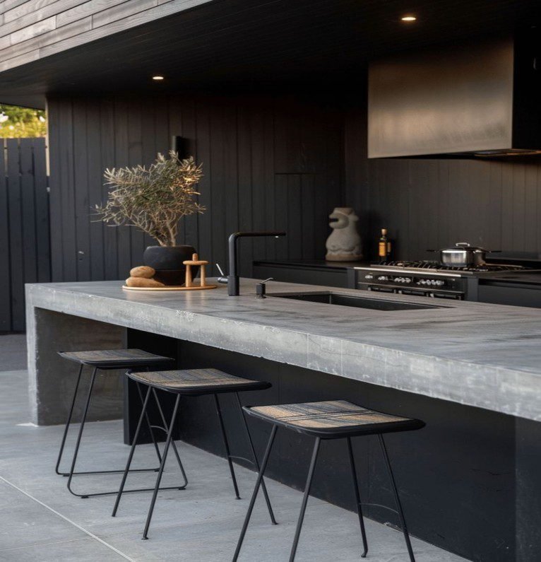 Industrial modern outdoor kitchen with dark uPVC cabinets, concrete counter, metal stools.