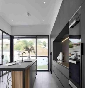 Modern minimalist kitchen with rattan-accented dark cabinets, large glass doors, airy layout.