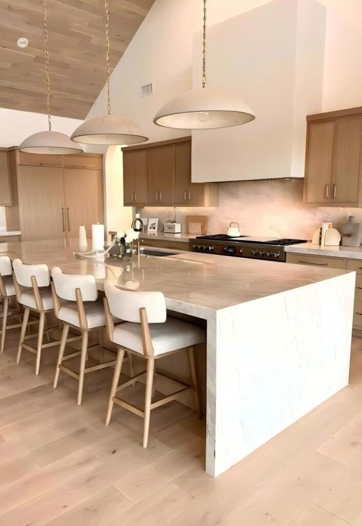Spacious modern farmhouse kitchen featuring a polished Taj Mahal Quartzite island paired with light oak cabinetry and vaulted wood ceilings.